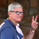 Apple CEO Tim Cook wearing a blue polo shirt walks by and makes the "peace sign" of to fingers held up to the camera.